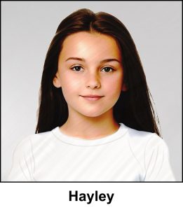 A watercolour painting of orphan Hayley, a sweet 8 year old girl, she has long brown hair and stunning hazel eyes tinged with a little green - in this relaxed pose she has a calm neutral expression with a hint of a smile - she is wearing a white T shirt against a greybackground - the image is labelled Hayley
